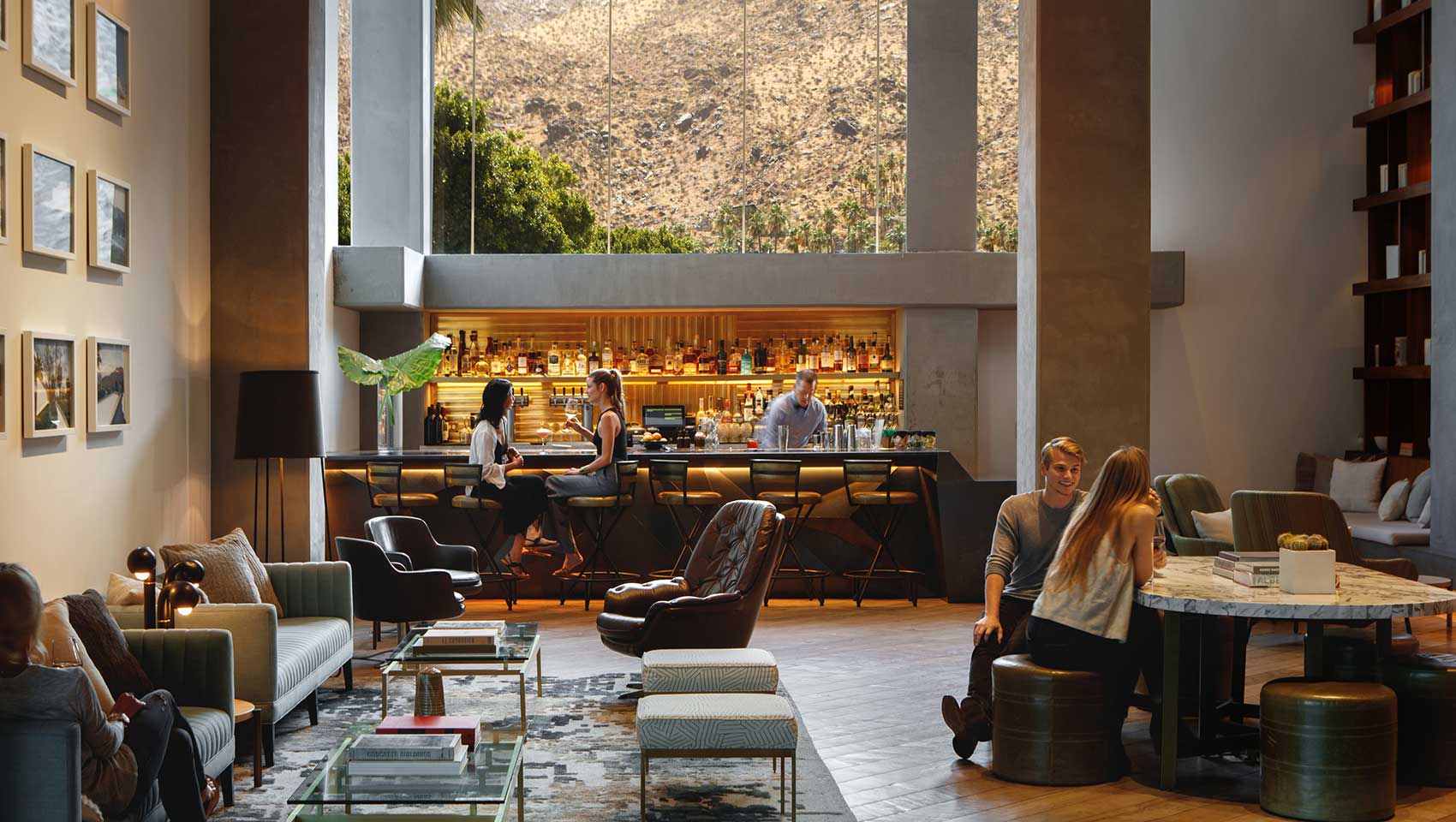 Lobby with backlit bar, people relaxing on sofas and chairs, and a tall window overlooking mountains